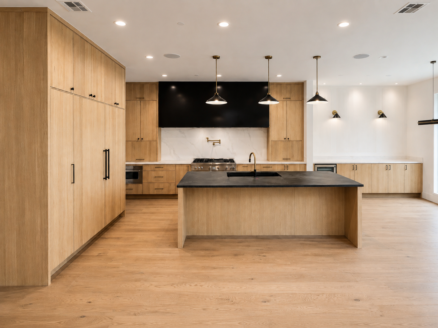 Modern luxury kitchen with light white oak cabinetry, black stone island and brass fixtures